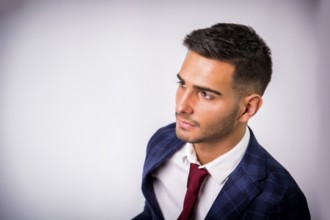 Handsome young man in blue business jacket and jeans posing on light background in studio