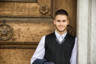 Elegant young man leaning against old wall and wooden door