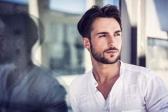 Stylish trendy young man standing outdoor against office window, looking confindent away