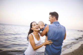 Beautiful young family on holiday with baby. The father holds the blonde girl in her arms, and the