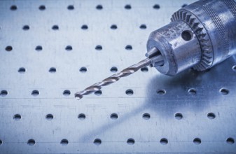 Metal drill on perforated metallic background construction concept