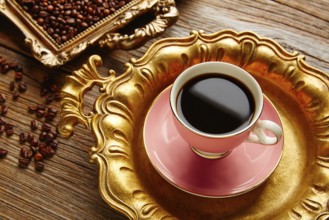 Coffee cup and beans on vintage golden tray in wooden old table