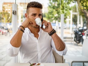 Close up of Handsome Young Man Drinking Coffee at the Shop While Talking on Cell Phone