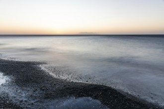 Morning atmosphere, sunrise over the sea, view from the lava beach to the island of Anafi, long