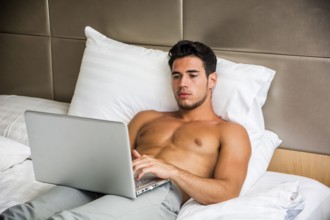 Attractive Young Shirtless Muscular Man with Serious Expression, Reclining Comfortably with Laptop