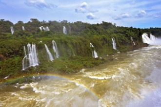 Raging and roaring water in the waterfalls of Iguazu. Turbid yellow-brown waves flow down. Above
