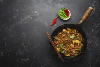 Stir fry soba noodles with chicken, vegetables in old rustic wok pan, chopsticks on black stone