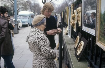 London 1982. A view from a London street with an elderly lady looking at art hanged on the fence to
