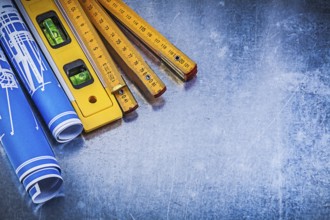 Blue rolled blueprints wooden meter construction level on metallic background
