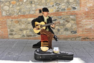 Granada, Andalusia, Spain, Europe, Musician playing guitar on the street next to an old stone wall,