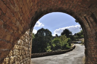 Domme in Perigord, View through a stone archway overlooking a curving path lined with trees under a