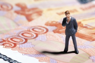 Miniature figurine businessman with 5000 rubles banknote on background. Concept
