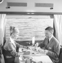 Train travel in the 1960s. A couple in the restaurant car of the train is enjoying dinner together.