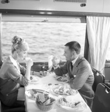 Train travel in the 1960s. A couple in the restaurant car of the train is enjoying dinner together.