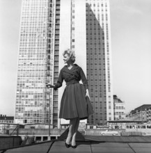 In the 1950s. A woman modelling a 1950s outfit with a jacket and skirt in matching dark. In the