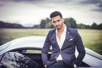 Portrait of young attractiave man in business suit sitting in his new stylish car outdoor in
