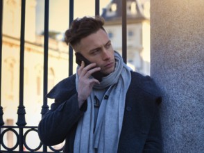 Handsome trendy man wearing white shirt standing and talking on cell phone, outdoor in city setting