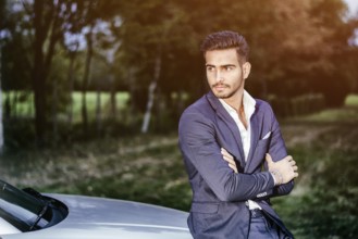 Portrait of young attractiave man in white shirt leaning on his new stylish polished car outdoor