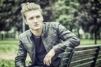 Handsome blond young man sitting on green, wooden park bench