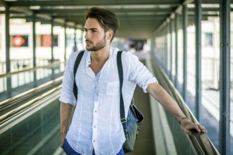 Handsome young man walking in city with backpack on shoulders, wearing white shirt