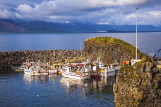 Sunset on the sea fjord in Iceland. White fishing boat in the harbor pier village Arnastapi