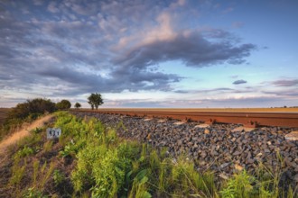 Old Railway tracks running through a field stretch to rural countryside at sunset. Single railway