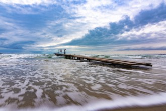 Sea landscape with beautiful clouds in blue tones, with a pier on the horizon