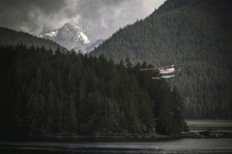 A seaplane flying over a forest and water with misty mountains in the background in Tofino on
