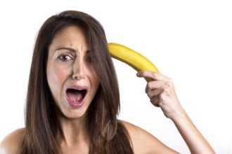 A funny portrait of a beautiful girl trying to shoot herself with a banana gun, while screaming.