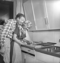 In the kitchen in the 1950s. Ayoung couple baking heart shaped gingerbread cookies for christmas.