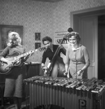 Trio 1956. The photograph, taken in 1956, captures three young women in a band, each immersed in