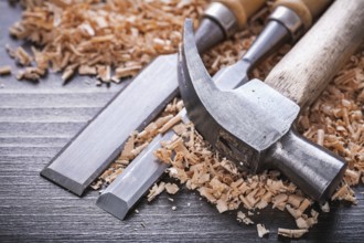 Close up of claw hammer and metal firmer chisels in wooden planning chips on vintage wood board