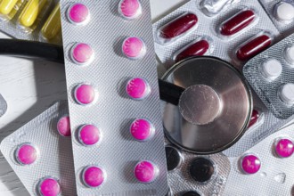Colorful pills in blisters are lying on the table next to the phonedoscope close-up