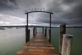 Wooden footbridge leads into a lake under a stormy sky, Allensbach, Untersee, Lake Constance,