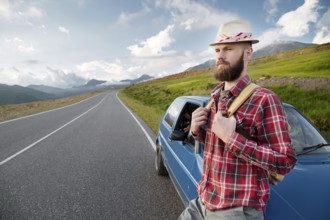 Attractive bearded man in a plaid red shirt and hat with a backpack. Stands next to a retro car on