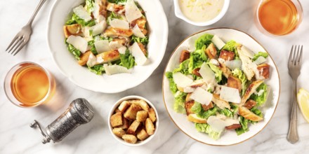Caesar salad panorama with the classic sauce and wine, shot from above on a white marble background