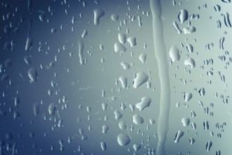 Close up of splashes of water and waterdrops running down on glass panel of bathtub in bathroom