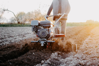 Person using a tiller on a farm field at sunrise, emphasizing farming and manual labor