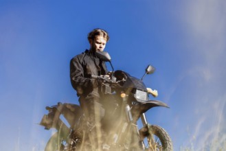 A young man in black clothing sitting on a motorcycle under a clear blue sky
