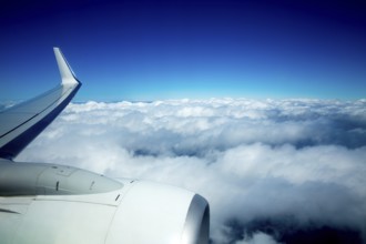 Airplane wing flying over fluffy clouds in blue sky high view