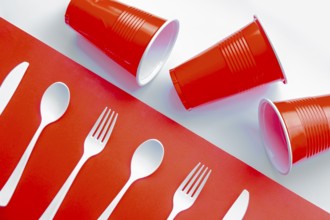 Horizontal view of single use white plastic cutlery and red plastic glass on a red and white