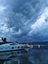 White motor yacht stands on the pier against the background of a twilight dark sky.