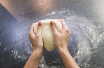 Woman preparing pizza dough on black granite table