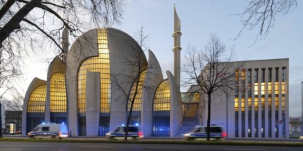 Several police vehicles with flashing lights drive past the Kölne Mosque in Ehrenfeld