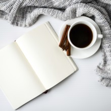 Cup of coffee with notebook cinnamon sticks and anise star on white background. Sweater around.