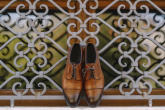 Stylish brown men's shoes made of genuine leather by the window with a metal lattice.