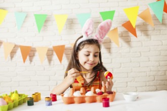 Girl with Easter bunny ears is painting colorful Easter eggs at home. Easter decorations and