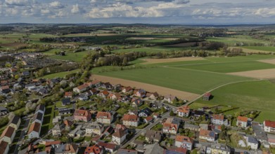 Aerial view of a neighbourhood with numerous houses and surrounding fields under a cloudy sky,
