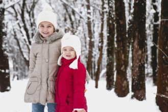 Cheerful little girls in warm clothes smiling and looking at camera while standing on snowy path in