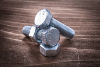 Couple of threaded metal bolts and screw nuts on vintage wooden board repairing concept